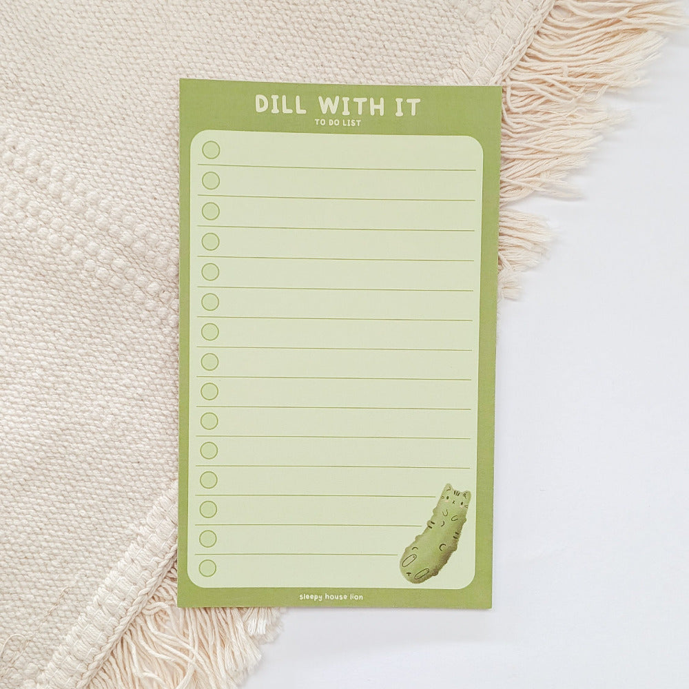 Green notepad with 'Dill With It' text and a dill pickle design on a textured surface.