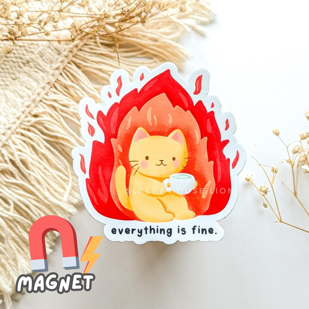 Magnet with a cat design holding a cup and 'everything is fine' text, on a textured surface.
