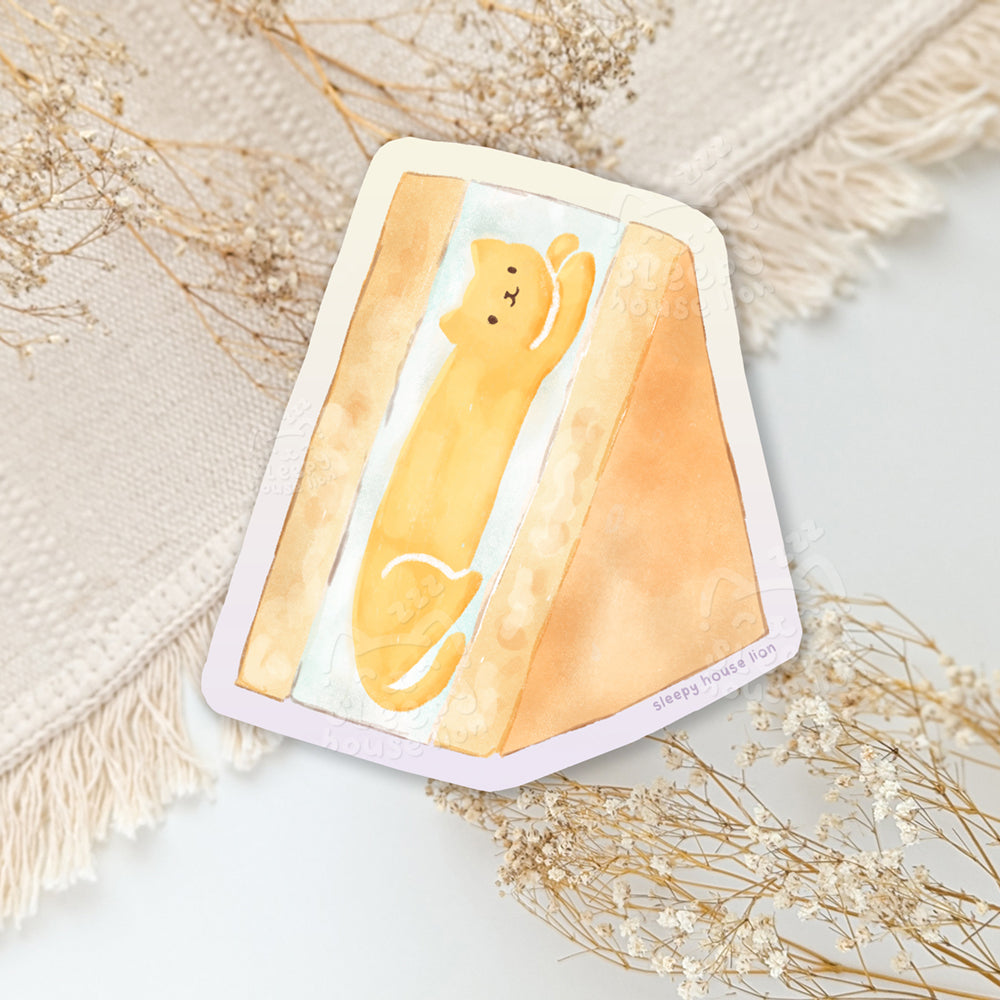 Sticker with a yellow cat mango sando on a textured surface with dried flowers