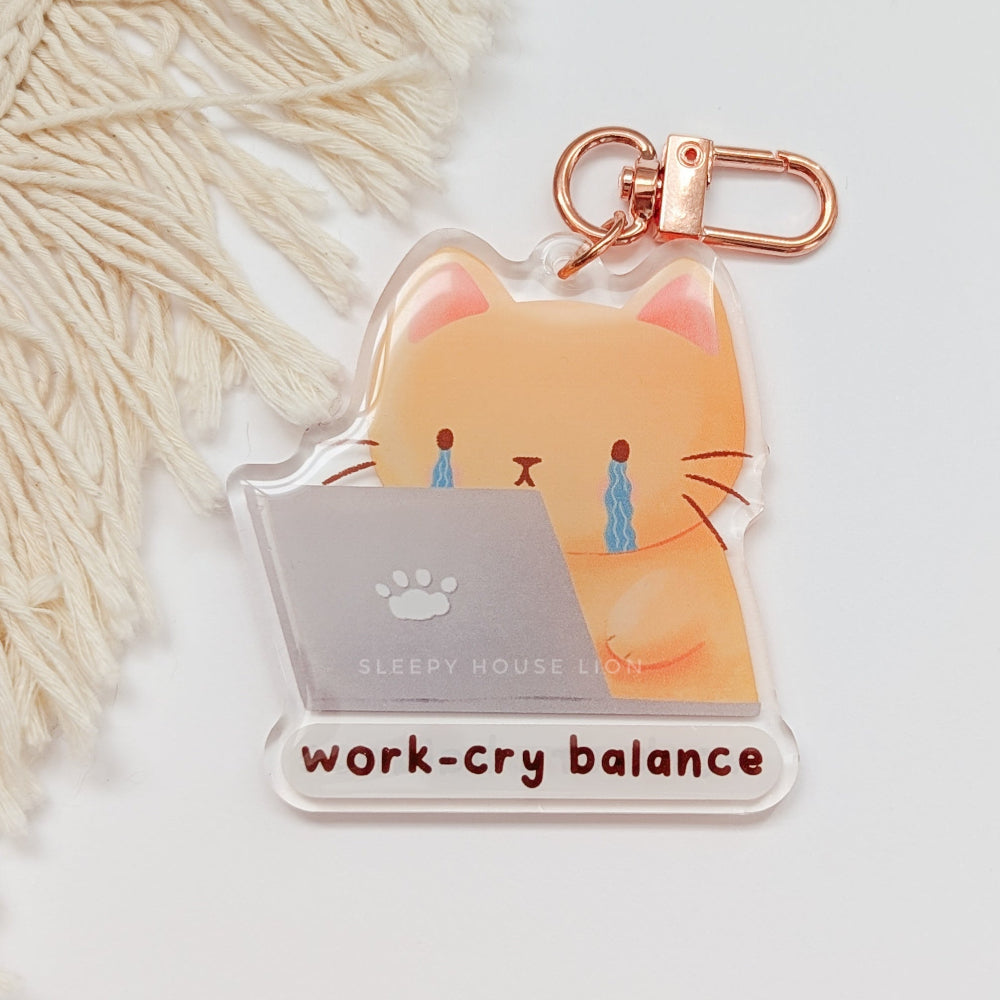 Keychain with a cat design and 'work-cry balance' text on a light background