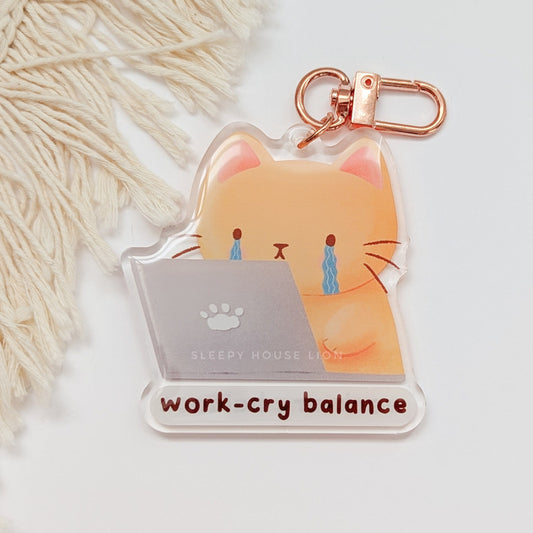 Keychain with a cat design and 'work-cry balance' text on a light background