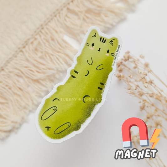 Green pickle-shaped magnet with a smiling face on a textured surface