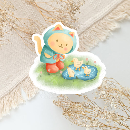 Sticker of a cat in a hood with ducks in a pond