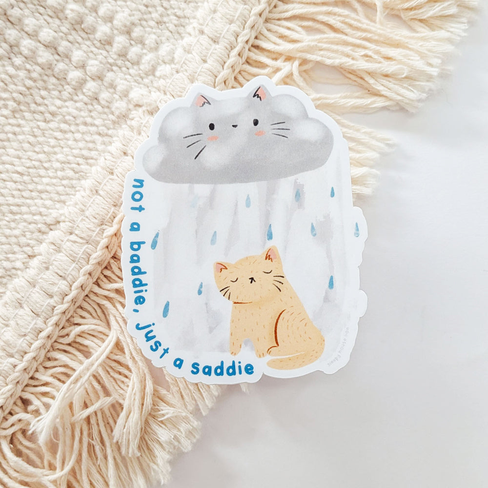 Sticker with a cat and cloud design with the text "not a baddie, just a saddie"