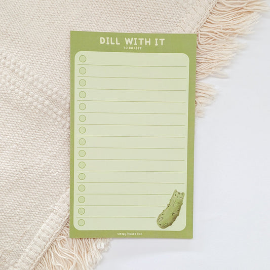 Green notepad with 'Dill With It' text and a dill pickle design on a textured surface.